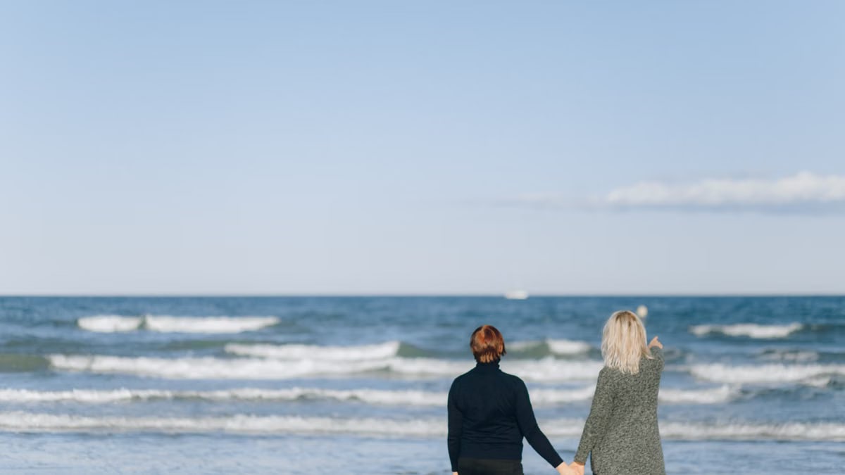 A romantic scene of a couple holding hands while enjoying a walk by the sea on a sunny day.